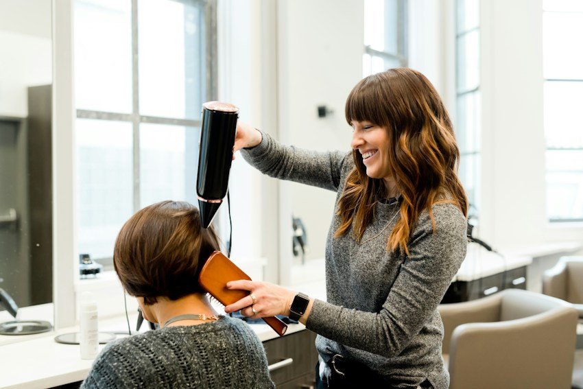 A smiling stylist doing a customer's hair in a bright salon